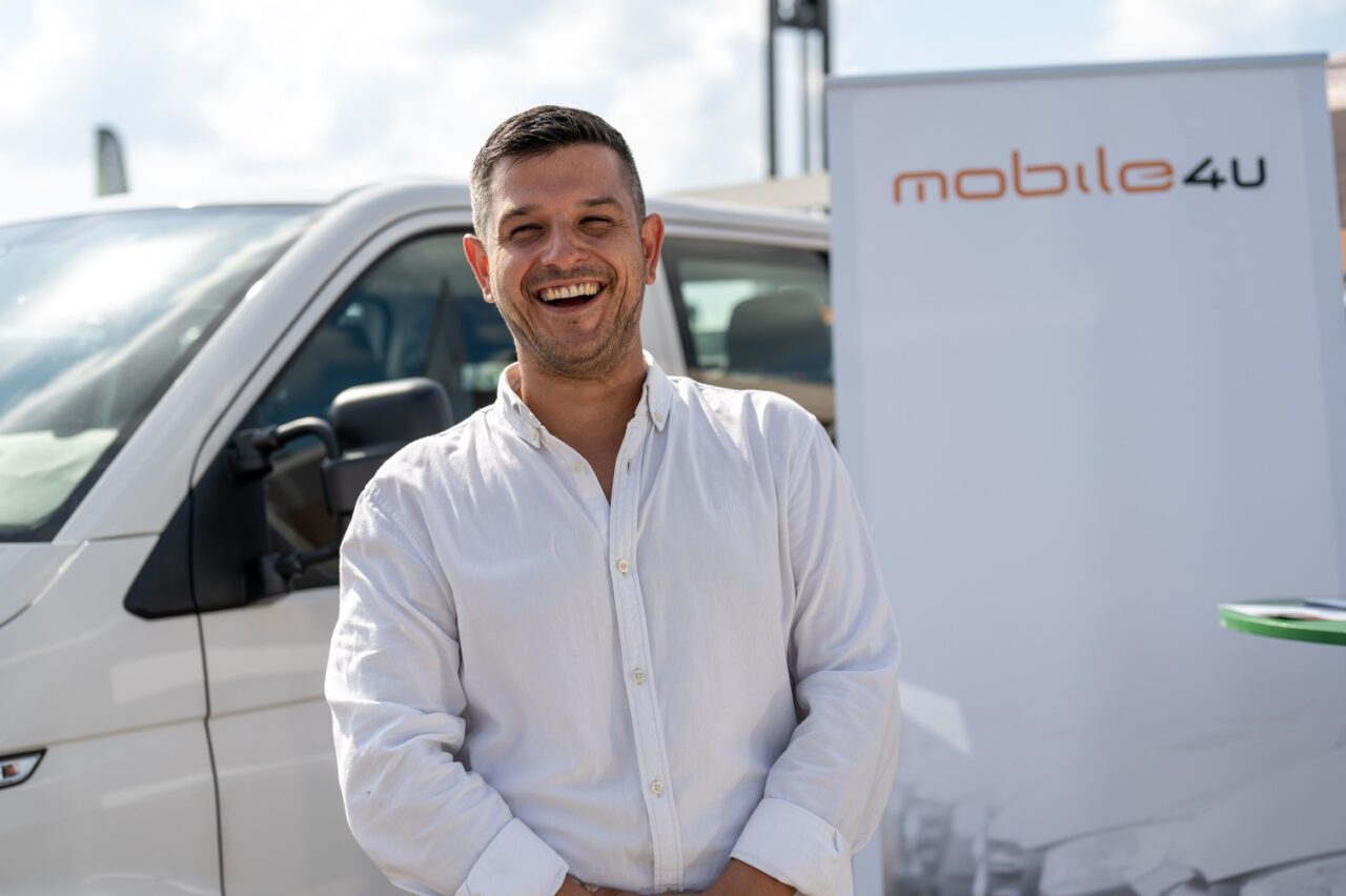Osoba stoji ispred automobila i roll-up plakata na sajmu